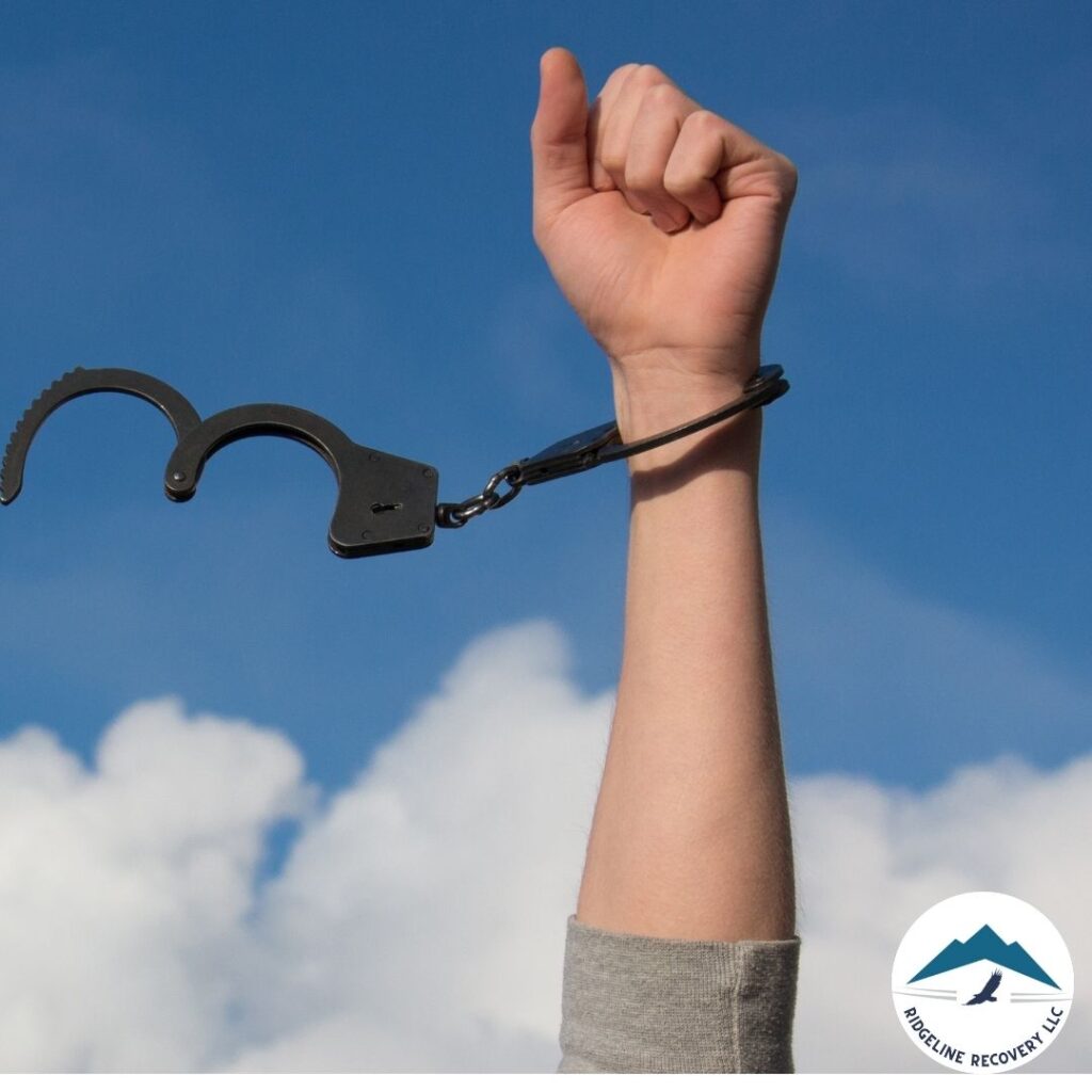 A hand breaking free from handcuffs against a blue sky, symbolizing the power of addiction therapy in achieving recovery in Columbus.