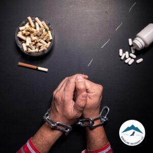 A person's hands are bound in chains, symbolizing the struggle of addiction, with cigarettes, pills, and drug paraphernalia nearby—illustrating the urgent need for a Detox Inpatient Near Me to begin the recovery process.