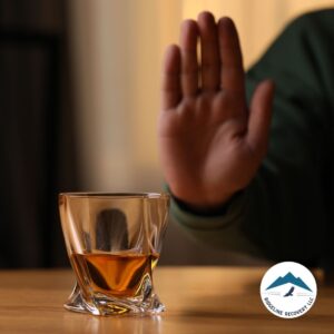 A close-up of a glass filled with alcohol on a wooden table, with a person in a green sweater raising their hand in refusal. This image symbolizes personal commitment to sobriety and the importance of Sober Houses in Columbus Ohio for a supportive and alcohol-free living environment.