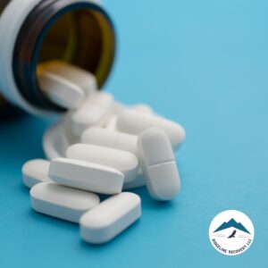 An open pill bottle spilling white tablets onto a blue surface, symbolizing prescription drug abuse and the need for a Detox Inpatient Near Me to support addiction recovery.