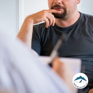 A man in a black t-shirt listens intently during a one-on-one counseling session, highlighting the importance of AA and NA meetings in Columbus, Ohio, for addiction recovery support.