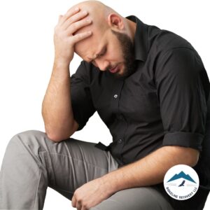 A distressed man in a black shirt sits with his head in his hand, symbolizing the emotional struggles of addiction recovery. Halfway House Columbus Ohio provides structured support, helping individuals rebuild their lives in a stable, sober environment.