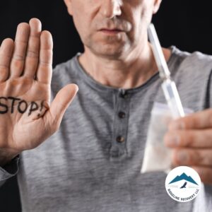 A man holds up his hand with "STOP!" written on it, rejecting a syringe and a bag of drugs, symbolizing the decision to seek a Detox Inpatient Near Me for addiction recovery.