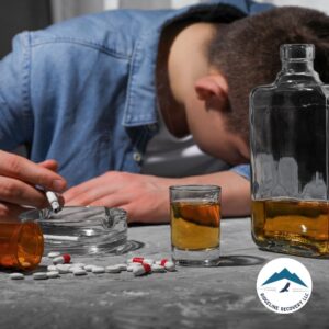 A man slumped over a table with pills, alcohol, and cigarettes around him, symbolizing the struggles of addiction and the need for Sober Living Rooms for Rent in Columbus.