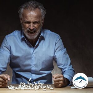 A distressed man clenches his fists and yells in frustration, surrounded by scattered pills—a powerful representation of the emotional struggle in Outpatient Rehab Columbus Ohio.