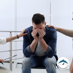 A distressed man sits with his head in his hands as two people place reassuring hands on his shoulders, symbolizing the emotional support offered in Outpatient Rehab Columbus Ohio.