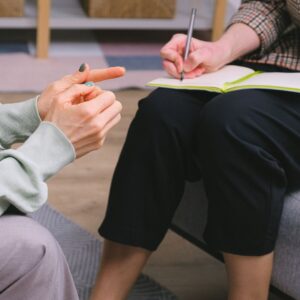 A client engaging in DBT therapy Columbus Ohio, using hand gestures while a therapist takes notes, focusing on emotional regulation and mindfulness techniques.