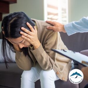 A distressed woman sits on a couch with her head in her hands, while a therapist offers reassurance with a comforting touch, symbolizing the compassionate care provided in Day Treatment Programs for addiction recovery and mental health support.