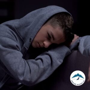 A young man in a hoodie resting his head on his arm, looking distressed, symbolizing the emotional struggles of addiction and the need for rehab for couples Ohio to heal and support each other.