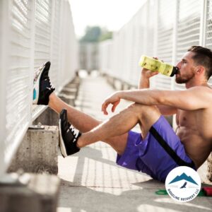 A fit man in athletic wear rests after a workout, drinking water, symbolizing strength and recovery through PHP Level of Care at Ridgeline Recovery in Ohio.