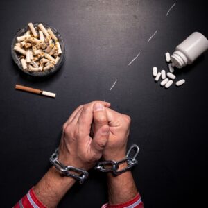 A pair of hands chained together, surrounded by cigarettes, pills, and drug residue, symbolizing the struggle of Effexor addiction and substance dependency.