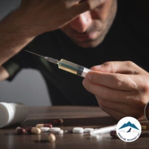 A distressed man holds a syringe while surrounded by scattered pills, symbolizing the struggle of addiction and the importance of Step 3 of Narcotics Anonymous in the journey to recovery.