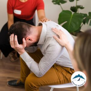 A distressed man sits in a therapy session with supportive hands on his shoulders, symbolizing the compassionate care provided through Inpatient Rehab Medicaid in Columbus, Ohio.