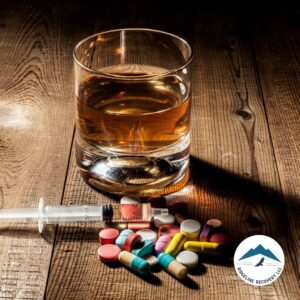 A glass of alcohol sits on a wooden surface next to a syringe and scattered pills, representing the dangers of substance abuse and the need for a detox from alcohol near me in Columbus, Ohio.