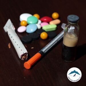 A collection of drugs, including pills, a syringe, and a vial, scattered on a dark surface, representing the struggle of addiction and the importance of Step 3 of Narcotics Anonymous in the recovery process.