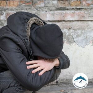 A person in a black hoodie crouches against a worn brick wall, head down in distress, symbolizing the challenges faced before entering Inpatient Programs for structured addiction recovery.