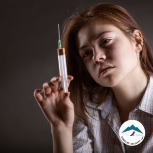 A young woman stares at a syringe, reflecting on the grip of addiction and the need for Court Mandated Substance Abuse Treatment as a path to recovery.