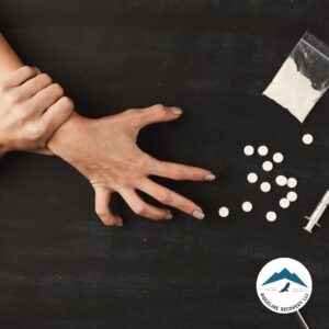 A person grips their wrist while experiencing the effects of drug addiction, with scattered pills, a syringe, and a bag of white powder nearby, emphasizing the urgent need for a detox from alcohol near me in Columbus, Ohio.