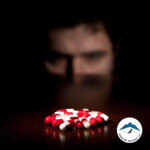 A distressed man stares at a pile of red and white capsules on a table, symbolizing the battle with addiction and the need for rehabs in Ohio that take Medicaid to provide accessible treatment.