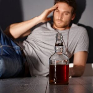 A distressed man sitting on the floor with a bottle of alcohol in front of him, symbolizing the dangerous effects of Effexor addiction and alcohol abuse.