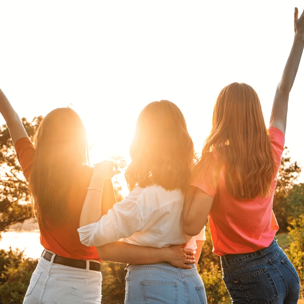 Three women standing together with their arms raised, symbolizing freedom, hope, and the positive impact of therapeutic behavioral services and day treatment programs.