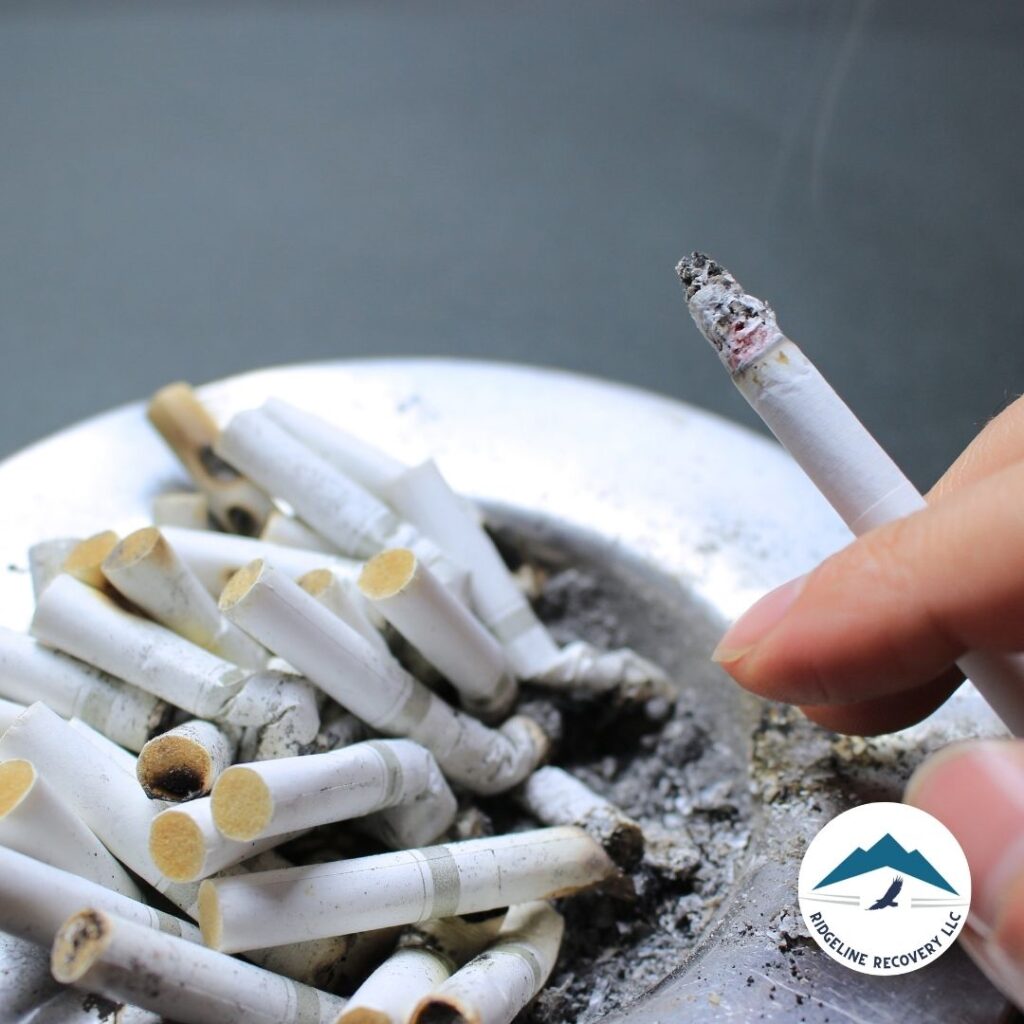 A hand holding a lit cigarette over an ashtray filled with cigarette butts, symbolizing addiction and the need for treatment.