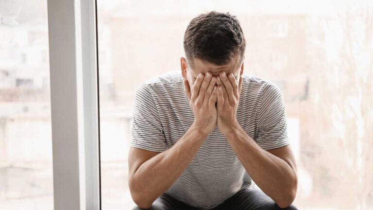 This image captures the heavy burden of modern life, depicting a man with his hands on his head, his face conveying deep worry and mental exhaustion.