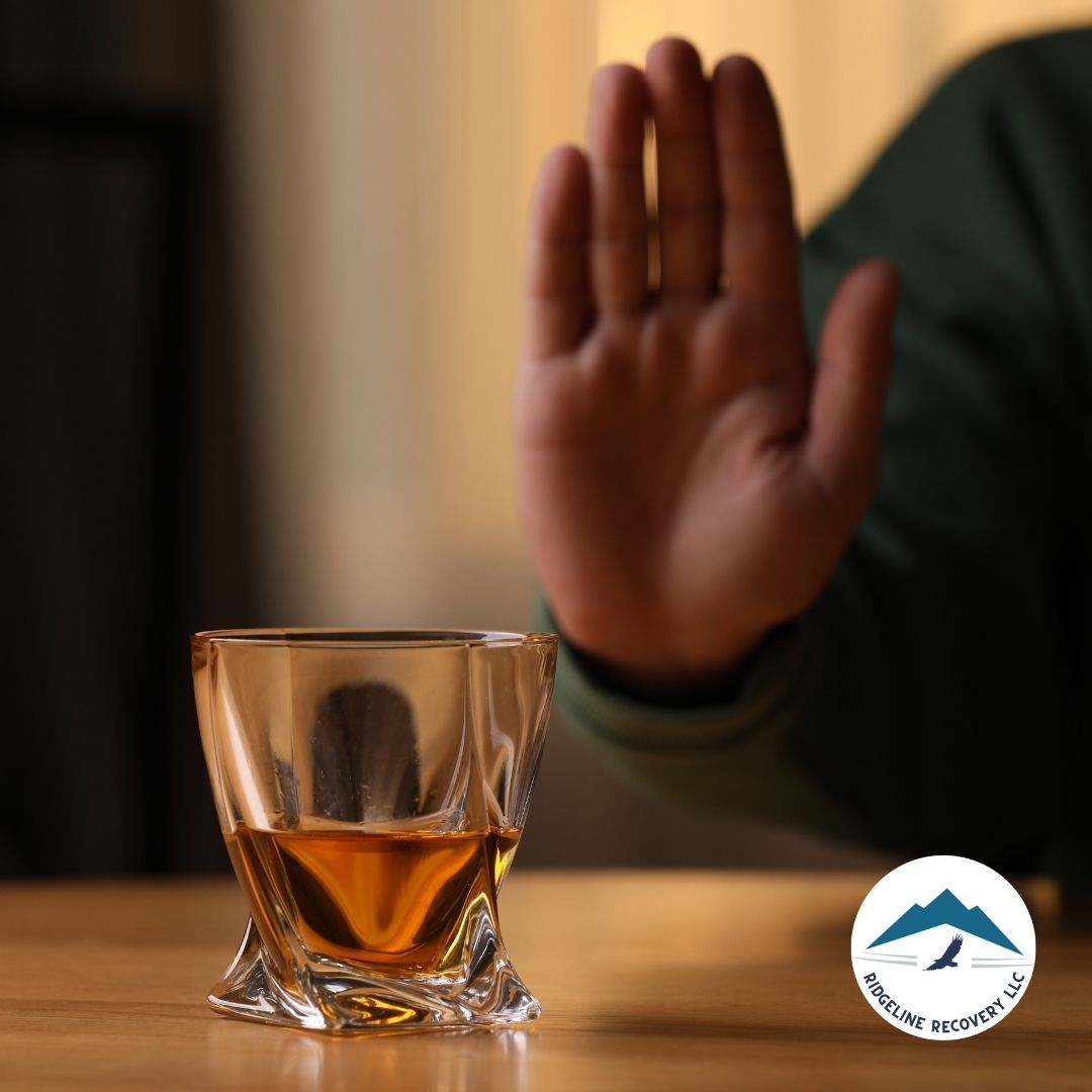 A close-up of a glass filled with alcohol on a wooden table, with a person in a green sweater raising their hand in refusal. This image symbolizes personal commitment to sobriety and the importance of Sober Houses in Columbus Ohio for a supportive and alcohol-free living environment.