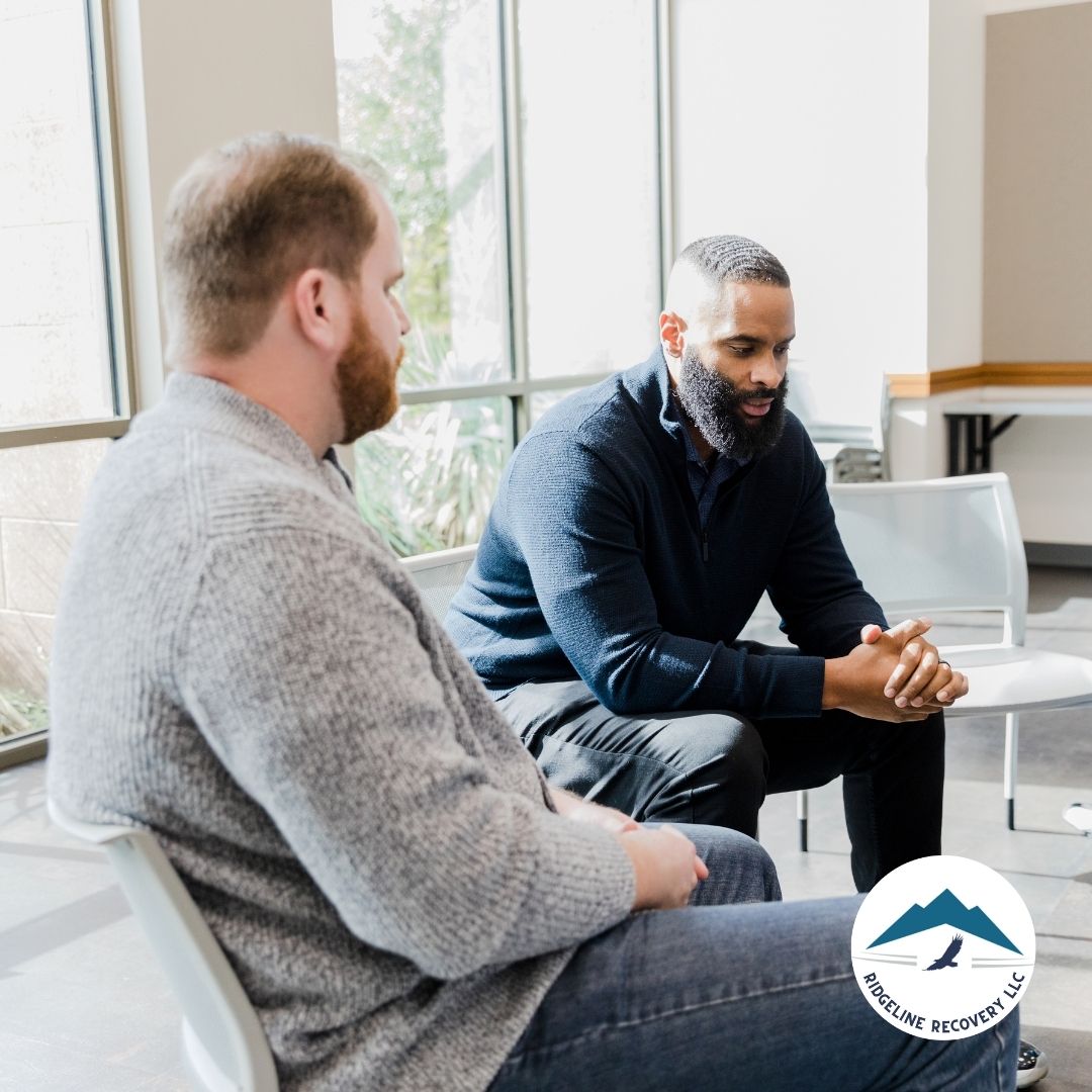 Two men sit in a bright, open space, engaged in a meaningful conversation. This image represents the NA 3rd Step, which encourages individuals to surrender control and trust in a higher power during their recovery journey.