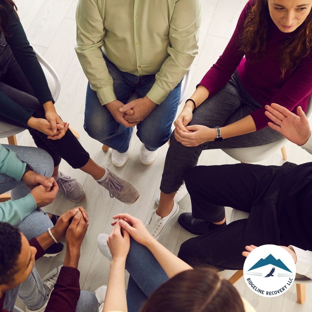 A group therapy session where individuals sit in a circle, hands clasped, engaging in discussion—a representation of the emotional and supportive process made possible through Casey Law, which allows families to seek mandatory addiction treatment for loved ones in need.