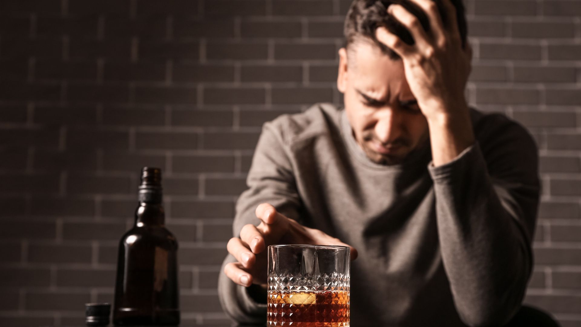 A man overwhelmed with stress and depression sits with a glass of alcohol, reflecting emotional and psychological causes of alcoholism.