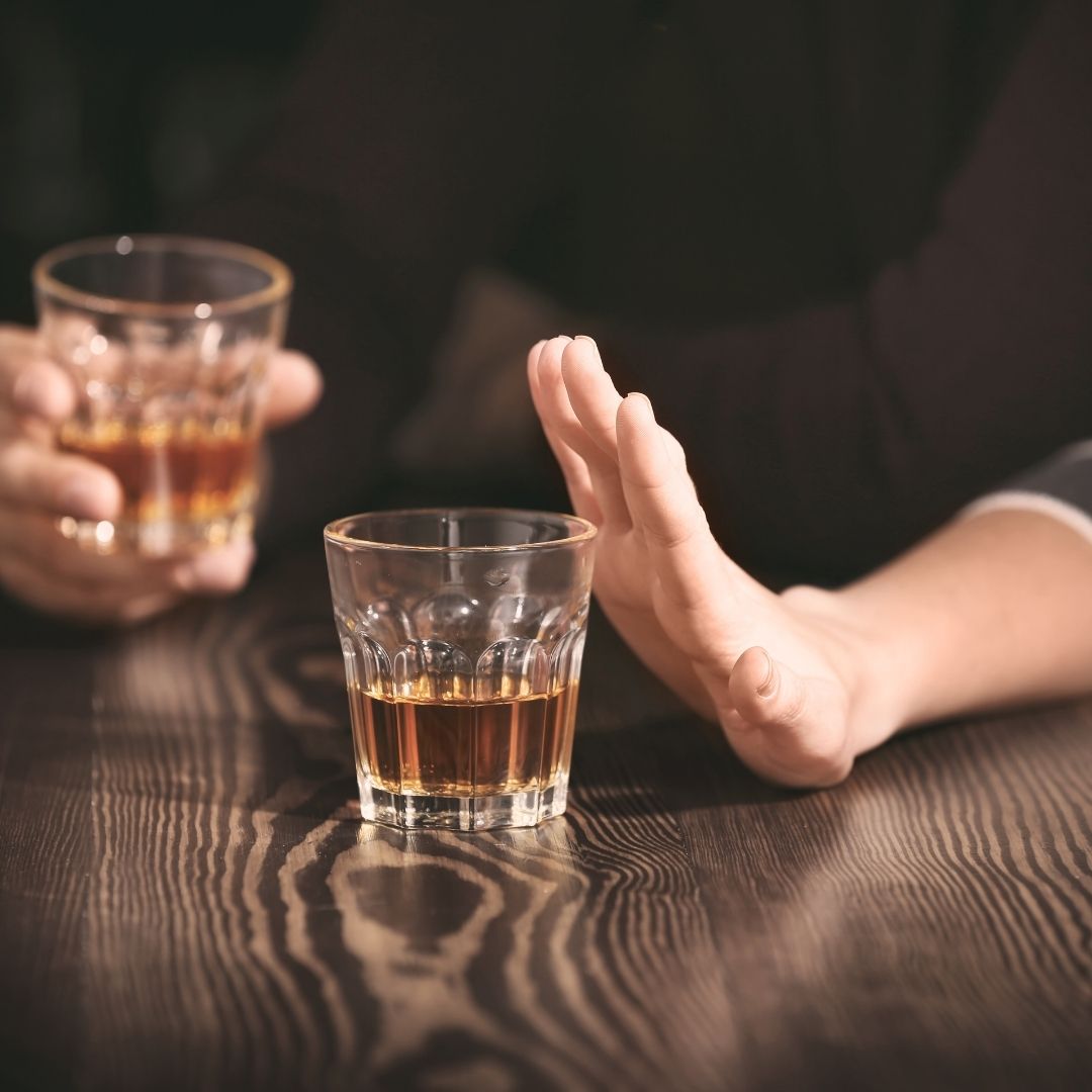 A person rejecting a glass of whiskey, symbolizing the importance of avoiding drinking on Accutane to prevent health risks and liver damage.
