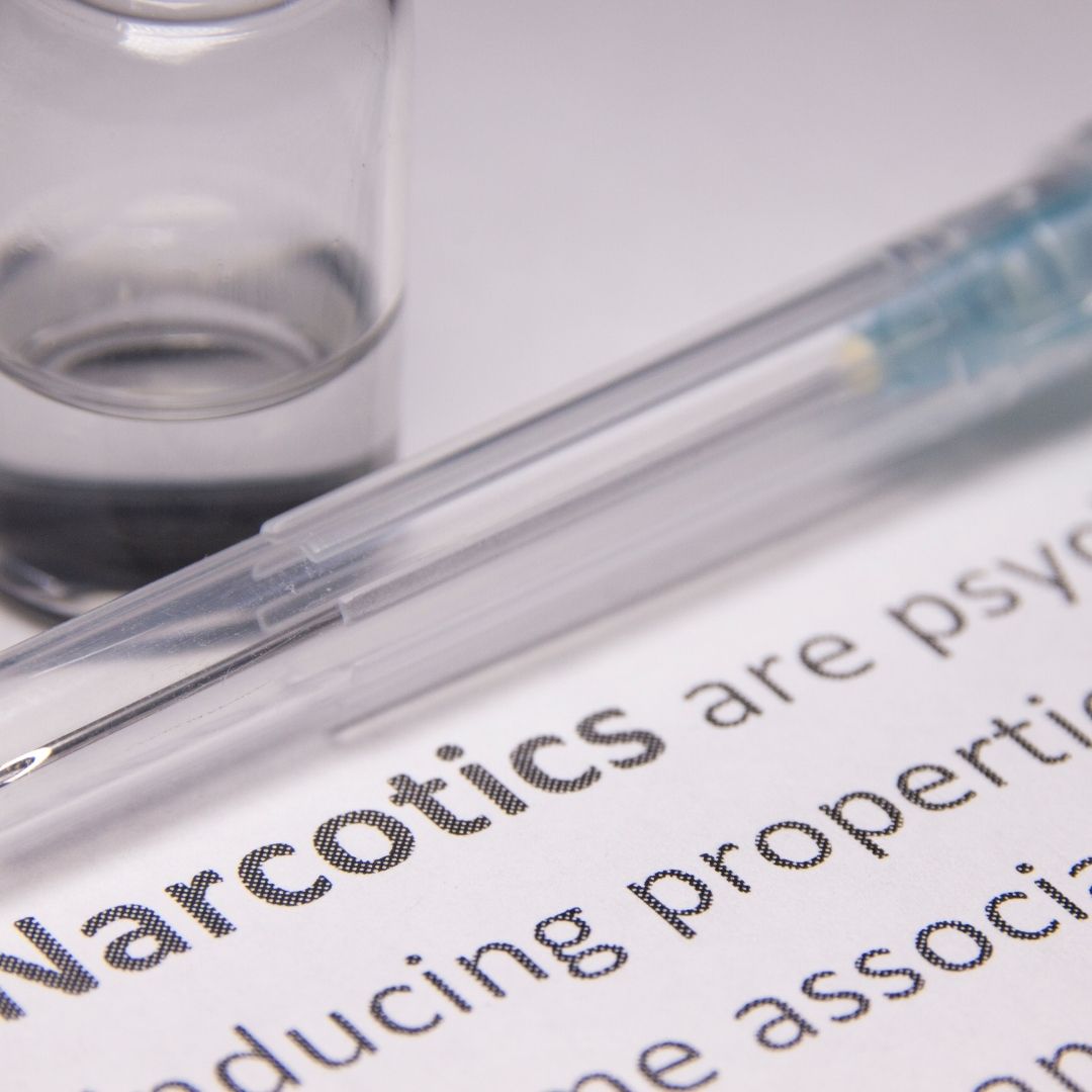 A close-up of the word "narcotics" on a printed document, with a syringe and medical vial in the background, illustrating the debate on is Xanax considered a narcotic and its legal status.