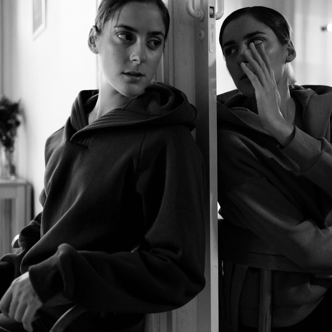 A woman sitting against a mirror, symbolizing the internal battle of powerlessness in addiction recovery, as she faces her reflection with uncertainty.