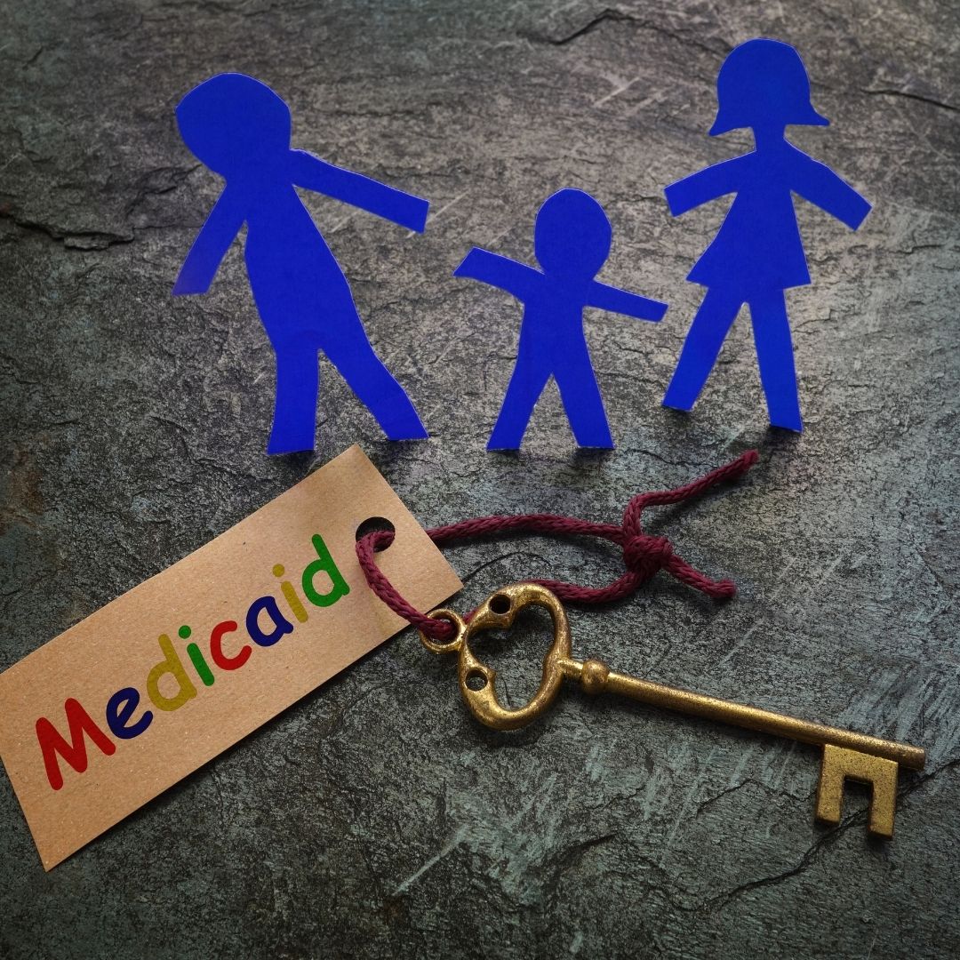 A symbolic image showing a Medicaid tag with a key and a paper-cut family, representing access to inpatient rehab that takes Medicaid near me, ensuring affordable addiction recovery for families in need.