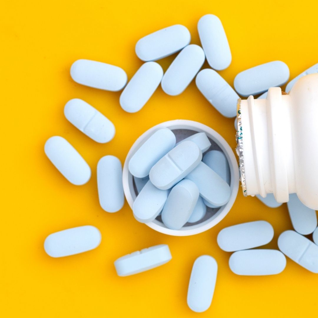 A white pill bottle spilling blue Meloxicam tablets onto a vibrant yellow background, raising questions about prescription medication safety and addressing the topic: Is the Drug Meloxicam Addictive?