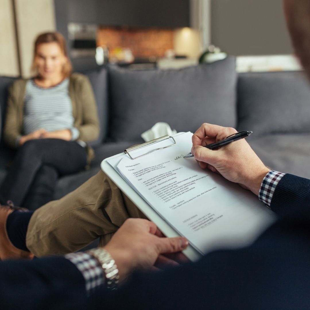 A therapist takes notes on a clipboard while a woman sits on a couch in a counseling session, illustrating the personalized treatment approach at a Methadone Clinic Columbus Ohio for opioid addiction recovery.