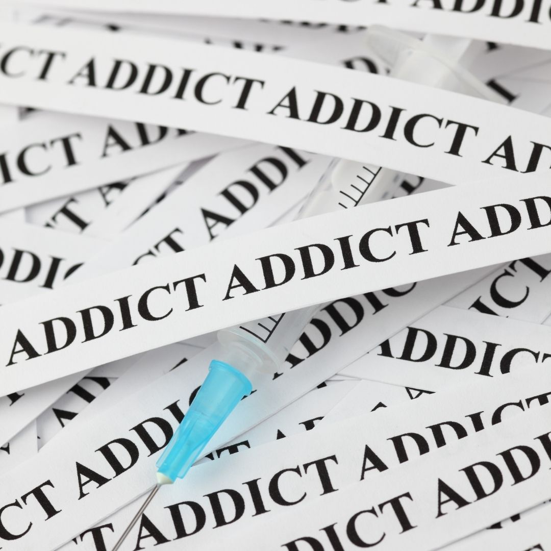 A scattered collection of white strips labeled "ADDICT" with a syringe underneath, symbolizing the stigma and struggle associated with Effexor addiction and substance dependence.