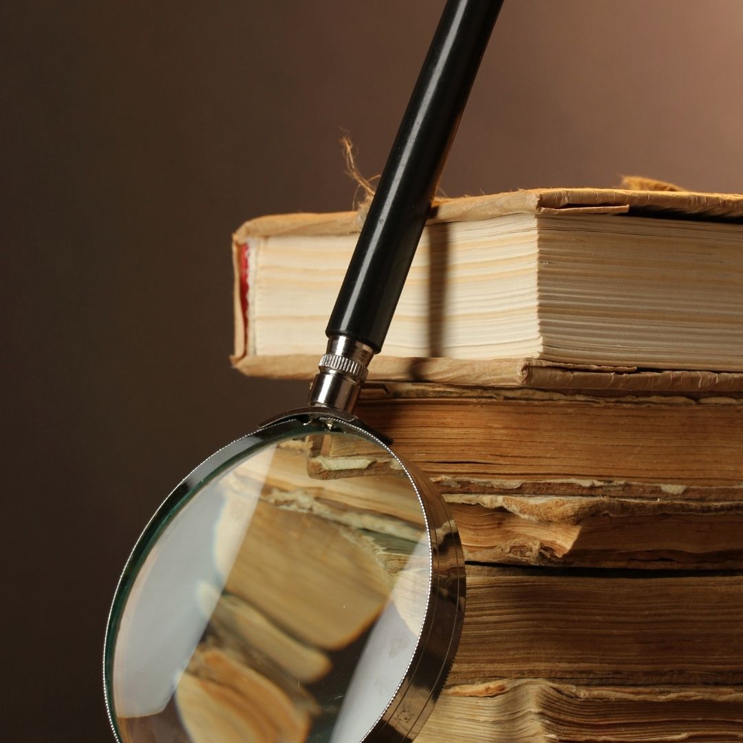 A magnifying glass resting on a stack of old, worn books, symbolizing the search for wisdom and deeper understanding found in the Refuge Recovery Book, a Buddhist-inspired guide to addiction recovery.