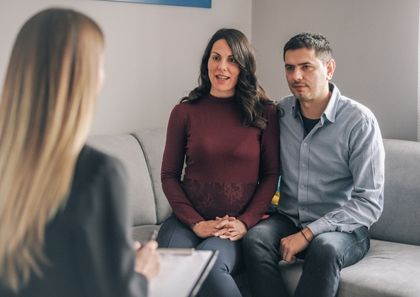 Addiction Therapy Services: A couple sitting on a couch talking to a therapist with a clipboard.
