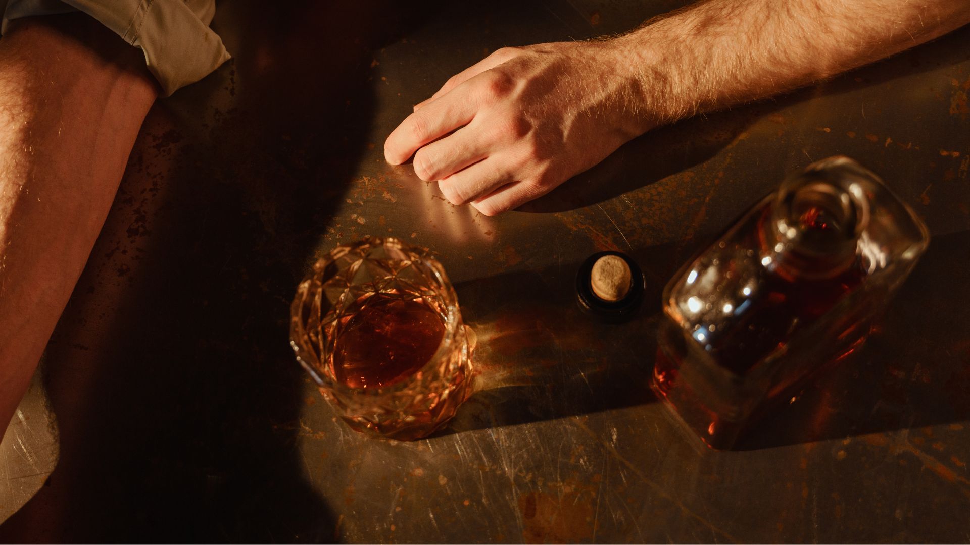 A man alone in a dark setting, holding a bottle, symbolizing emotional weight and dependence on alcohol contributing to drug and alcohol addiction.