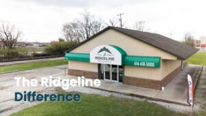 A clean, professional shot of the Ridgeline Recovery facility exterior, featuring a visible address and phone number (614-618-5000) on the green awning. The building represents a dedicated center for addiction services. The text overlay, "The Ridgeline Difference", emphasizes the specialized approach to treatment, including available Medication-Assisted Treatment (MAT) programs.