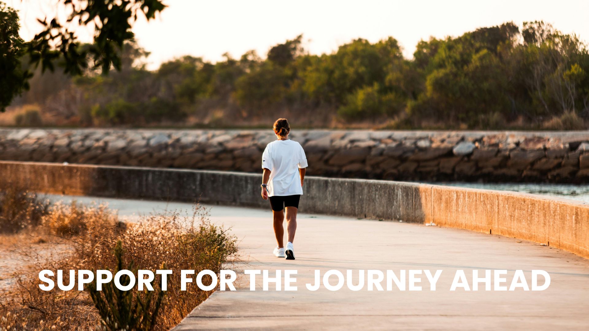 How to Help a Recovering Alcoholic. A woman walking alone on a concrete path by a river at sunset with text overlay reading "Support for the Journey Ahead," focused on how to help a recovering alcoholic.