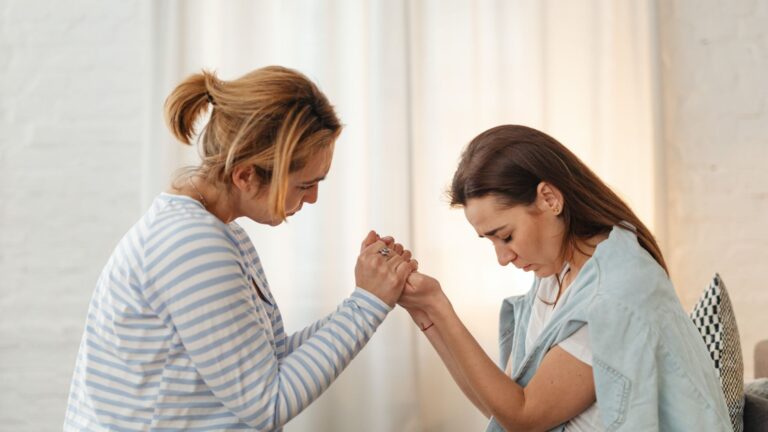 Two women sitting together and holding hands in a supportive gesture during a substance abuse treatment session.